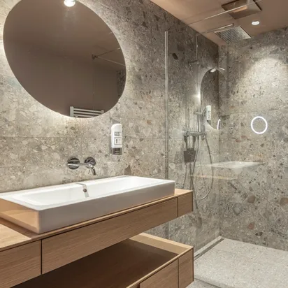 Modern bathroom with terrazzo walls, walk-in shower, large round mirror, and wooden vanity